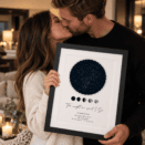 Couple kissing while holding a personalised star map print in a cozy setting.